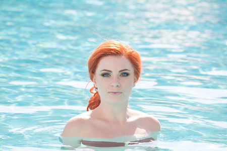 Portrait of a beautiful woman getting out of a swimming pool. beautiful long hair tanned model posing by blue pool water. Outdoor summer portrait of sexy girl in sunglasses. woman in red swimsuit.の写真素材
