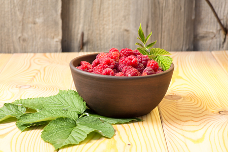Fresh organic healthy raspberry with mint leaves in clay dish on wooden table background. Rustic style and natural light. food photo.の写真素材