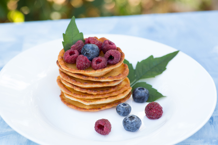 A stack of delicious pancakes with sour cream, raspberries and blueberries on a light background. with copy spaceの写真素材