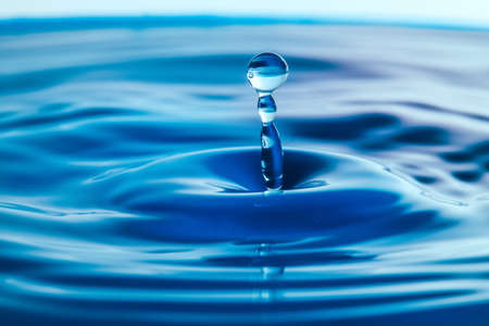 Dark blue water droplets splash close up on the water surface. It creates a water wave and a perfect crownの写真素材
