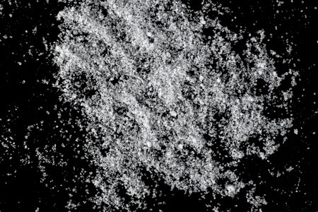 Close-up of white sugar isolated on black background, top view lying down.