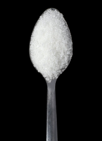 Close-up of white sugar on a spoon. isolated on a black background. top view lying downの写真素材