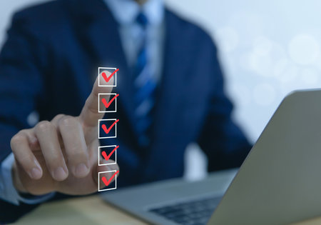 Businessman hand holding a pen ticking a red checkmark on a box in the list Show on the virtual screen. Checklist Ideas in Business Survey items and questionnaires. copy spaceの写真素材