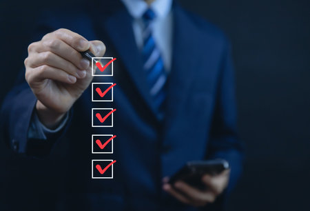 Businessman hand holding a pen ticking a red checkmark on a box in the list Show on the virtual screen. Checklist Ideas in Business Survey items and questionnaires. copy spaceの写真素材