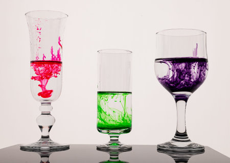Backlit and reflecting surface scene of different food colouring dye droplets falling down into...