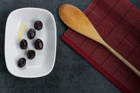 Black olives in a white bowl and wooden spoon on a black backgroundの写真素材