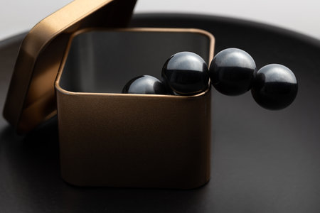 Minimalist close-up of a metallic box with glossy black magnetic spheres emerging from it, creating a modern and abstract visual aesthetic.の写真素材