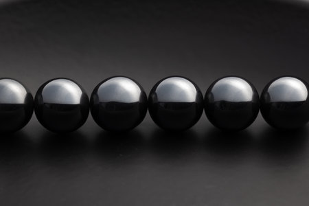 Minimalist close-up of shiny black magnetic spheres aligned in a row on a dark surface, creating a sleek and modern abstract composition.の写真素材
