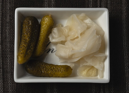 Close-up shot of pickled cucumbers and sliced pickled cabbage served in a white ceramic dish, captured on a dark textured background. Ideal for food, fermentation, and culinary theの写真素材