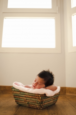 Sweet newborn sleeping at a basket with a window behindの写真素材
