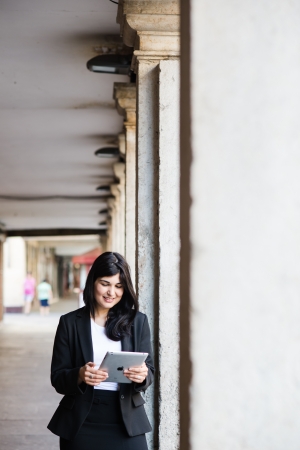 Pretty brunette smiling and surfing on a tablet in the streetの写真素材