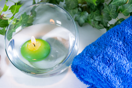 Lit candle with some leaves and a blue towel, in a bathroom or a spa, with white backgroundの写真素材
