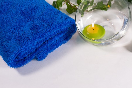Lit candle with some leaves and a blue towel, in a bathroom or a spa, with white backgroundの写真素材
