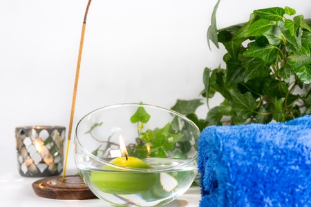 Lit candle with incense, some leaves and a blue towel, in a bathroom or a spa, with white backgroundの写真素材