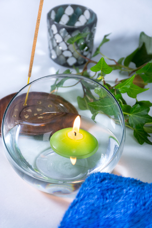 Lit candle with incense, some leaves and a blue towel, in a bathroom or a spa, with white backgroundの写真素材