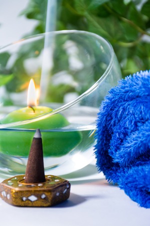 Lit candle with incense, some leaves and a blue towel, in a bathroom or a spa, with white backgroundの写真素材
