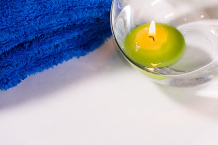 Lit candle with a blue towel, in a bathroom or a spa, with white backgroundの写真素材