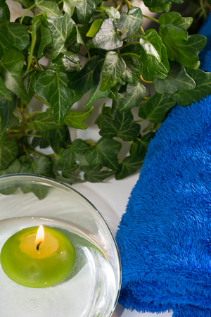 Lit candle with some leaves and a blue towel, in a bathroom or a spa, with white backgroundの写真素材