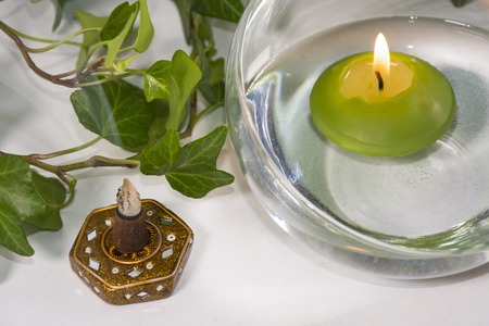Lit candle with incense and some leaves, in a bathroom or a spa, with white backgroundの写真素材