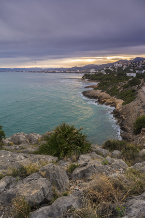 Benicassim town and beach from a hill at north, at sunset, with rocks at foregroundの写真素材