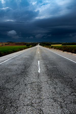 Old straight section of an asphalt road between cereal fields with a storm in the backgroundの写真素材