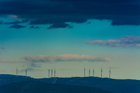 Some towers of wind mills on the mountains under a overcast sky with black cloudsの写真素材