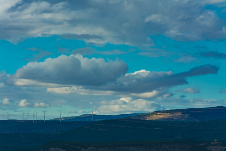 Some towers of wind mills on the mountains under a overcast sky with white cloudsの写真素材