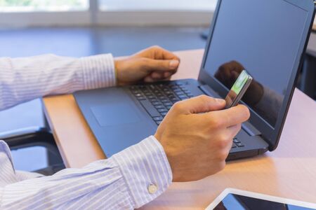 Businessman with fingers on a smartphone with a laptop and a tablet on the tableの写真素材
