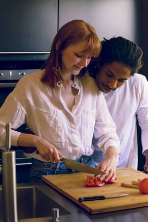 An interracial couple preparing vegetables in the kitchen while huggingの写真素材