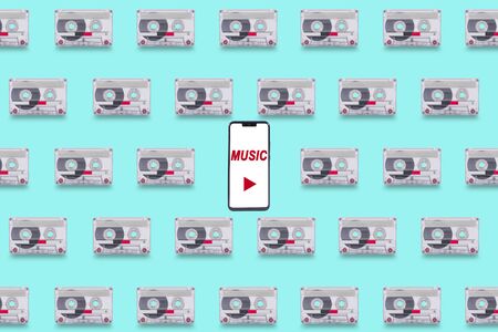 Background with old cassette tapes in tile format, with a smartphone in the center as a concept of comparison between old and new media deviceの写真素材