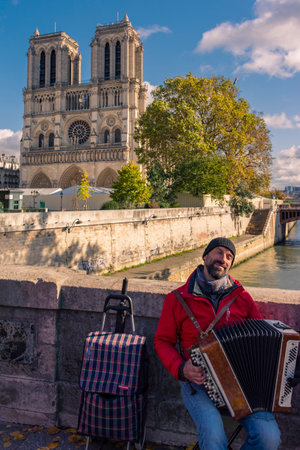 Paris, France - November 7, 2019: A street musician plays the accordion on the Des Coeurs bridge (of the Hearts) in front of the Notre Dame cathedralのeditorial素材