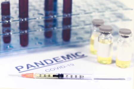 Syringe and vaccine vials with a test tube holder. Paper with the word pandemic and covid-19. Virus, vaccine and treatment conceptsの写真素材
