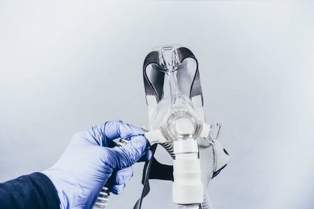 Hand with medical glove holding respiratory mask for sleep disorders isolated. White background. Apnea. Medical devices. Air pump. Assisted breathing. Copy spaceの写真素材