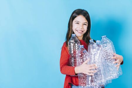 A little girl with plastic bottles on a blue background. Concept of environmental care, recycling, reuse and reduce, plasticfreeの写真素材