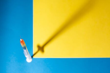 Syringe for vaccine or insulin, with its shadow, on a blue and yellow background. Spot or selective focus. Concepts of health, vaccination, coronarivus or drugsの写真素材