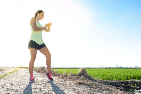 A young sportswoman girl happily checks the statistics on her watch after practicing running on the fieldの写真素材