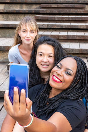 Group of smiling young women of diverse races sharing fun moments using smartphone. Concepts like diversity, friendship, companionshipの写真素材