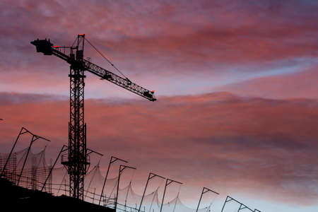 Silhouette of a crane and top of a building under construction with orange sky and clouds at sunset or sunriseの写真素材