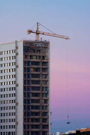 A crane and a building under construction with blue and purple sky at sunset or sunriseの写真素材