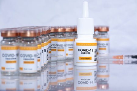 Spanish coronavirus vaccine for intranasal use in inhaler with out-of-focus vials and syringe in the background, looking like a laboratory or health centerの写真素材