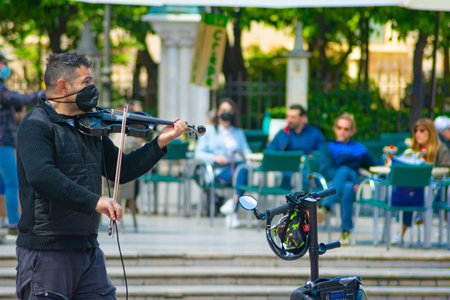 Valencia, Spain, April 17, 2021: Busker with his violin, entertaining tourists, in one of the main squares of the city, with many terraces of bars and restaurants. Defocused people at backgroundのeditorial素材