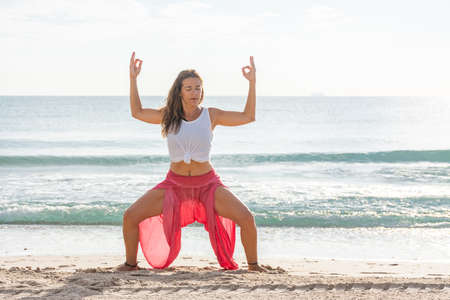 Woman on the beach doing the yoga posture konasana utkata, with the sea at backgroundの写真素材
