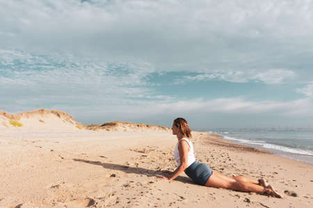 Woman on the beach doing the sun salute yoga posture or Surya Namaskara, at sunsetの写真素材