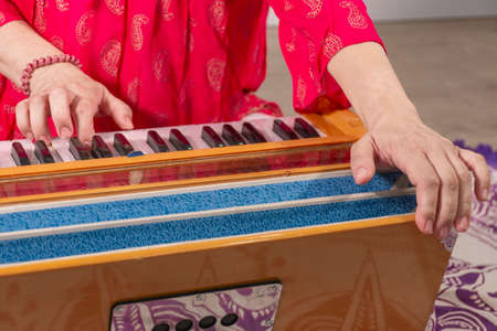Hands of woman in red traditional dress sitting on the floor playing the harmonium in a kundalini yoga practiceの写真素材