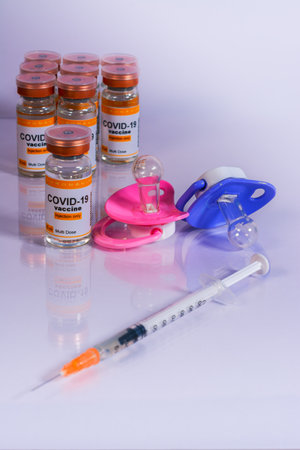 Baby pacifiers next to vials and syringe with the coronavirus vaccine. Child vaccination conceptの写真素材