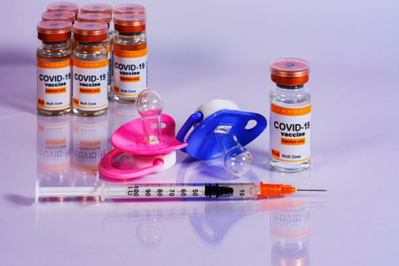 Baby pacifiers next to vials and syringe with the coronavirus vaccine. Child vaccination conceptの写真素材