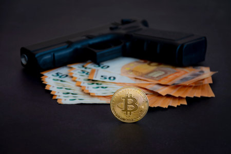 Bitcoin coin in the foreground with a gun and euros, defocused in the background, in the dark. Photography and studio lightsの写真素材