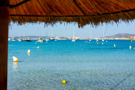 Moored sailboats at the Xinxell cove, and Palmanova at background, from the sand, next an umbrellaの写真素材