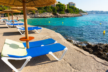 Cala Comtesa cove, Ses Illetes, Majorca, Balearic Islands, Spain. July 20th, 2022 - Umbrellas and loungers on a terrace bar on the rocky coast in front of the seaのeditorial素材