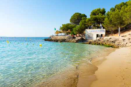 Cala Comtesa cove, Ses Illetes, Majorca, Balearic Islands, Spain. July 20th, 2022 - Bar terrace with umbrellas at a pinewood next to the sand. Translation: Balearic school of canoeingのeditorial素材